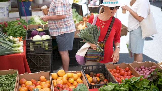 A woman browses boxes of fresh fruits, vegetables and kale at the Farmers Market in Sonoma, California on a bright morning.