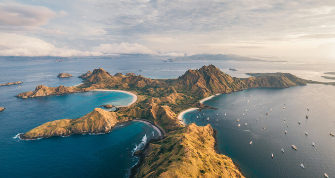 Aerial view of Padar Island featuring rugged hills and three distinct crescent-shaped bays with turquoise water under a soft sky, Komodo, East Nusa Tenggara, Indonesia.