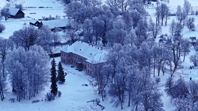 Aerial view of historic manor house surrounded by snow-covered trees and fields in winter in Latvia.