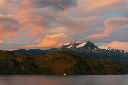 View of Lake Pehoe with snow-capped mountains under a vibrant sunset sky with pink clouds in Torres del Paine, Magallanes and Chilean Antarctica, Chile.