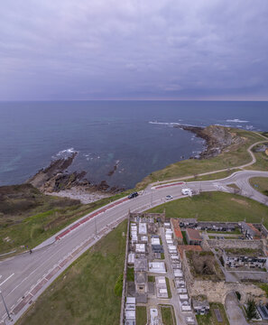 Aerial view of the historic cemetery of Comillas situated on a cliff overlooking the Cantabrian Sea with a coastal road winding through the green landscape in Comillas, Cantabria, Spain.