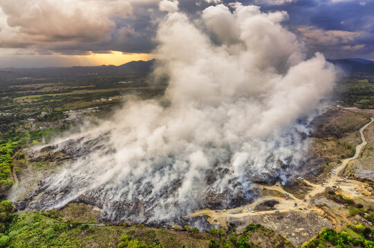 Aerial view of the Vertedero Duquesa landfill with thick smoke rising from burning waste, surrounded by rural landscape and dirt roads in Pantoja, Santo Domingo, Dominican Republic.