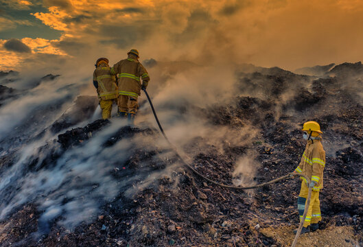 Aerial view of firefighters battling a large fire at the Vertedero Duquesa landfill with thick smoke rising under a golden sunset sky in Pantoja, Santo Domingo, Dominican Republic.