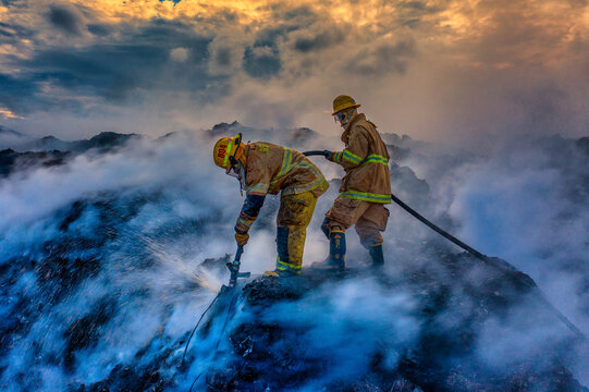 Aerial view of firefighters working to extinguish a large fire at the Vertedero Duquesa landfill, with thick smoke and water spray in Pantoja, Santo Domingo, Dominican Republic.