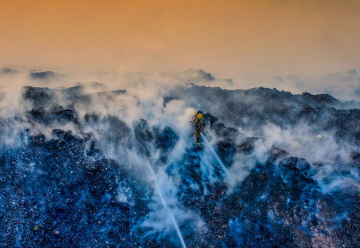 Aerial view of firefighters battling a large fire at the Vertedero duquesa landfill with thick smoke rising into the orange sky in Pantoja, Santo Domingo, Dominican Republic.