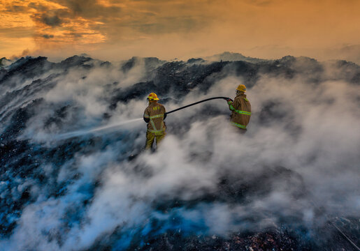 Aerial view of firefighters working to extinguish a large fire at the Vertedero Duquesa landfill with thick smoke rising into the sky during sunset in Pantoja, Santo Domingo, Dominican Republic.