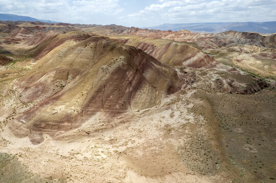 Tuzluca, Turkey - 04 July 2025: Aerial view of Igdir Rainbow Hills with colorful striped sedimentary rock formations and arid landscape under a cloudy sky.