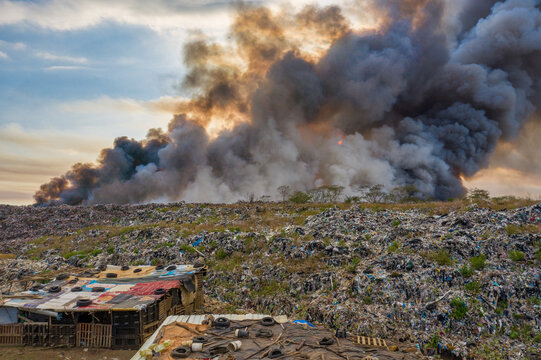 Aerial view of Vertedero Duquesa landfill with thick smoke billowing into the sky above makeshift dwellings in Pantoja, Santo Domingo, Dominican Republic.