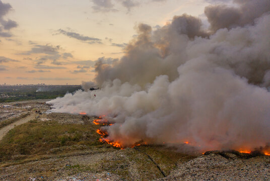 Aerial view of the fire at Vertedero duquesa landfill with thick smoke billowing into the sky and a helicopter flying overhead in Pantoja, Santo Domingo, Dominican Republic.