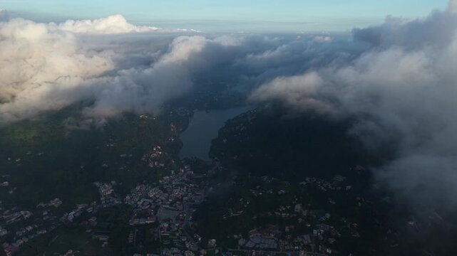 Aerial view of Bhimtal lake surrounded by lush green hills and town buildings partially obscured by clouds in Bhimtal, Uttarakhand, India.