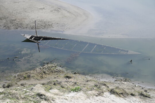 Gaibandha District, Rangpur Division, Bangladesh - 15 July 2026: View of a partially submerged wooden boat in the river near Char Krishnamani, with sandy banks and calm water.