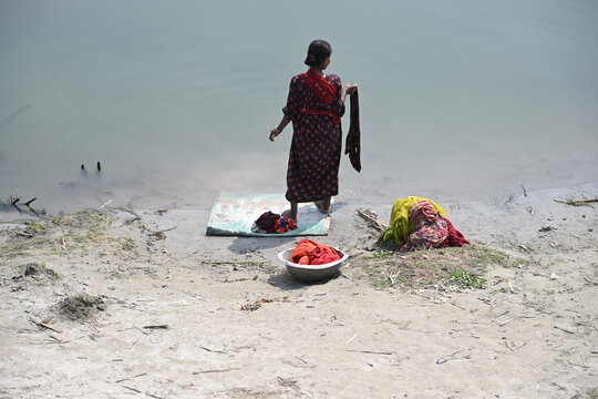 Gaibandha District, Rangpur Division, Bangladesh - 15 July 2026: View of a woman washing clothes at Char Krishnamani, with colorful garments on the sandy riverbank.