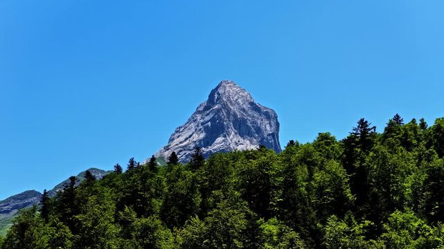 Aerial view of Col d'Aubisque mountain peak rising above a dense green forest under a clear blue sky in Beost, Nouvelle-Aquitaine, France.