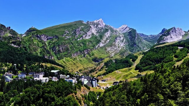 Aerial view of the Col d'Aubisque mountain pass with rocky peaks, lush green slopes, and a small village nestled in the valley in Beost, Nouvelle-Aquitaine, France.