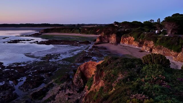 Aerial view of Plage de la Marche aux Boeufs at sunset with rocky cliffs, sandy beach, and calm sea in Asserac, France.