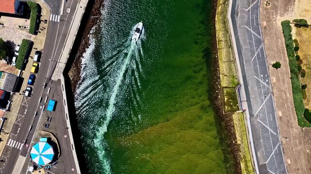 Aerial view of Port de Capbreton with boat wake in green water, parking area, and striped umbrella in Capbreton, Nouvelle-Aquitaine, France.