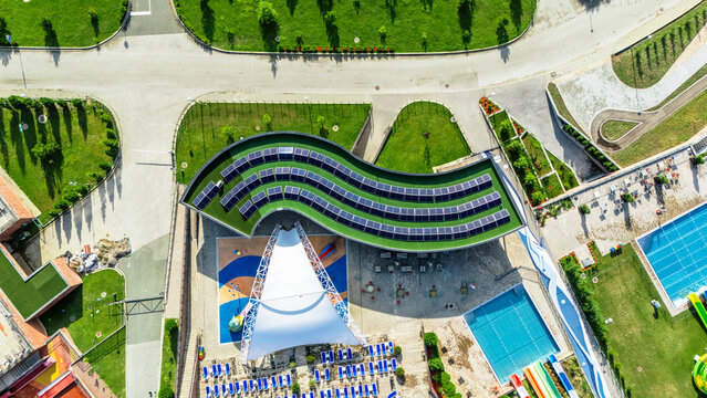 Aerial view of Movenpick Resort Spa Fruske Terme with a curved solar-paneled roof, white tensile canopy, and swimming pools in Vrdnik, Vojvodina, Serbia.
