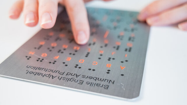 A blind woman learns the English alphabet from a braille sign.