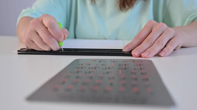 A blind woman writes in Braille using a stencil on a piece of paper. 