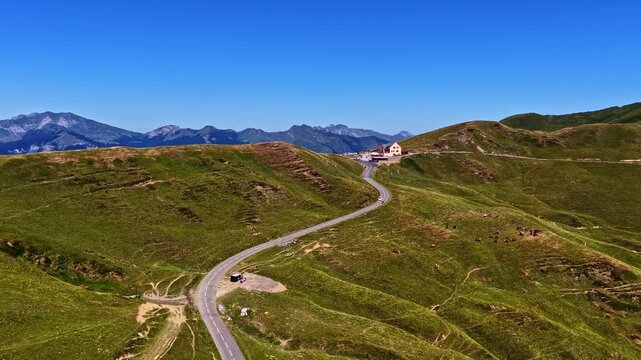 Aerial view of the winding mountain road at Col d'Aubisque, surrounded by lush green slopes and rolling hills under a clear blue sky in Beost, Nouvelle-Aquitaine, France.