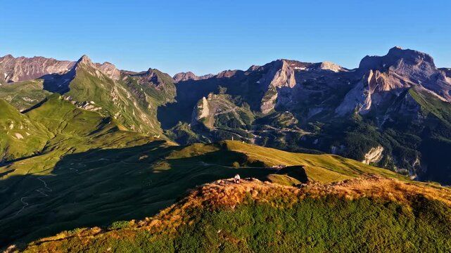 Aerial view of a hiker standing on the ridge of Col d'Aubisque surrounded by green mountain slopes and rocky peaks in Beost, Nouvelle-Aquitaine, France.