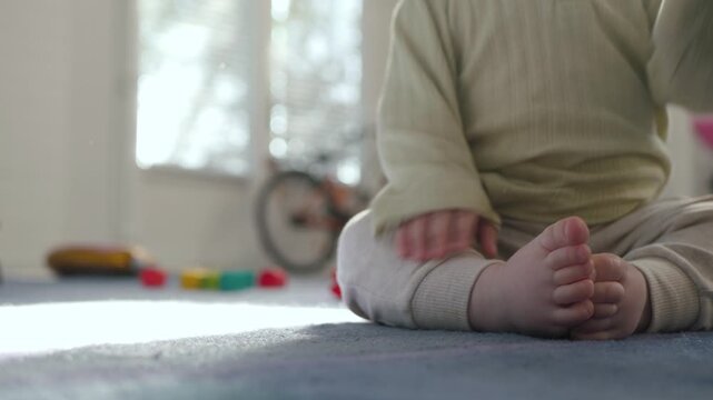A truly touching moment, an unrecognizable baby sits on the carpet and tries to take his first exciting steps, receiving loving support from his parents in a cozy, inviting indoor environment