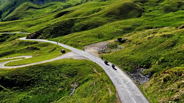 Aerial view of Col d'Aubisque winding road with motorcyclists riding through lush green mountain slopes in Beost, Nouvelle-Aquitaine, France.