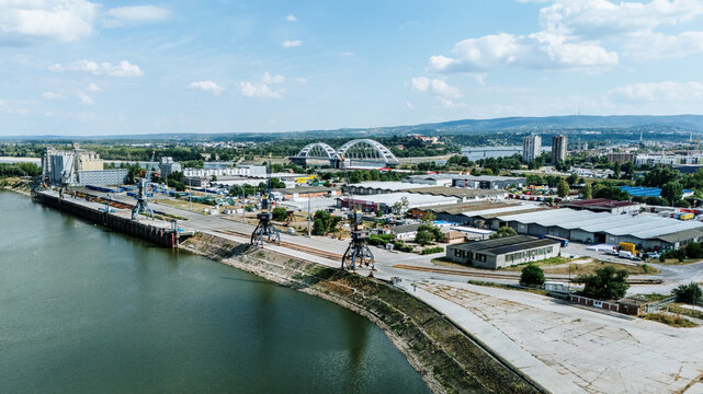 Aerial view of Luka Novi Sad port facilities on the Danube river, featuring industrial cranes, warehouses, and the Zezelj Bridge in the background, Novi Sad, Vojvodina, Serbia.