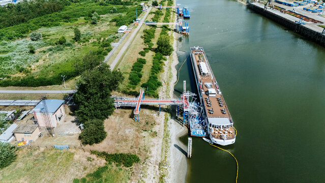 Aerial view of Luka Novi Sad with a large cruise ship docked at the river port, featuring industrial infrastructure, green banks, and calm water in Novi Sad, Vojvodina, Serbia.