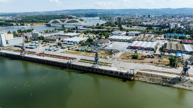 Aerial view of Luka Novi Sad port on the Danube river with industrial cranes, warehouses, and the Zezelj Bridge in the background in Novi Sad, Vojvodina, Serbia.
