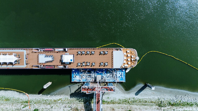 Aerial view of a river cruise ship docked at Luka Novi Sad with outdoor seating on the deck and a yellow floating barrier in the Danube river in Novi Sad, Vojvodina, Serbia.