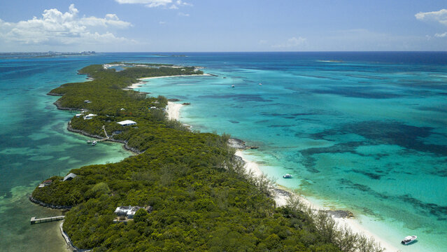 Aerial view of a lush tropical cay surrounded by turquoise waters, white sandy beaches, and dense vegetation in Nassau, New Providence, The Bahamas.