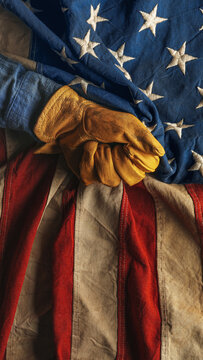 Hand in worn work glove holding the American flag. Symbolic of hardworking blue collar workers, USA manufacturing, pride in products Made in United States of America, or to celebrate US Labor Day.