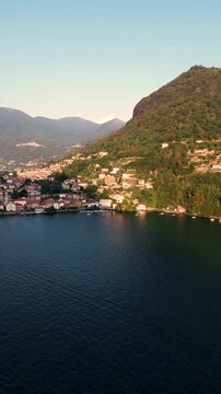 Aerial view of the village of Torno on the shores of Lake Como, with historic stone buildings and lush green hillsides reflecting in the water, Torno, Lombardy, Italy.