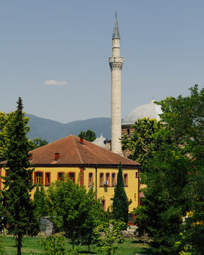 View of the historic Mustafa Pasha Mosque with its slender minaret and dome rising above a yellow building and lush green trees in Skopje, Greater Skopje, North Macedonia.