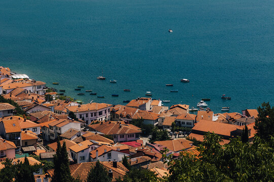View of Lake Ohrid with its historic town featuring terracotta rooftops and small boats floating on the blue water in Komuna e Ohrit, North Macedonia.