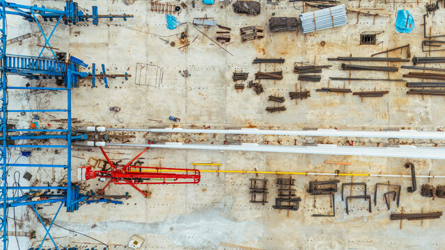 Aerial view of a construction site featuring a red crane, organized steel beams, and various building materials on a concrete foundation in Novi Sad, Serbia.