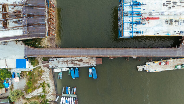 Aerial view of a bridge construction site over the Danube river with various small boats docked along the bank in Novi Sad, Serbia.