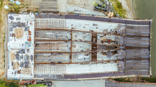 Aerial view of a bridge construction site featuring extensive steel reinforcement bars, concrete foundations, and wooden scaffolding along the riverbank in Novi Sad, Serbia.