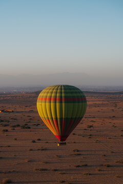 View of a colorful hot air balloon floating over the arid desert landscape near the Atlas Mountains at sunrise in Marrakesh, Marrakesh-Safi, Morocco.