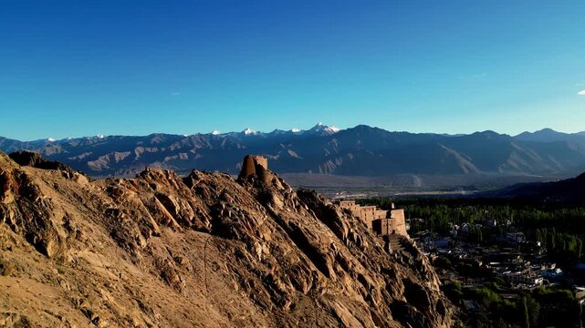Aerial view of Leh Palace perched on a rocky ridge with the Himalayan mountain range in the background under a clear blue sky in Leh, Ladakh, India.