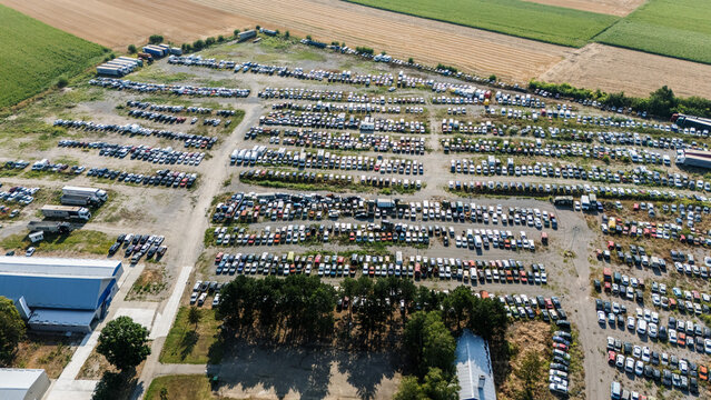 Aerial view of a large outdoor vehicle storage lot filled with rows of parked cars and trucks, surrounded by agricultural fields in Vojvodina, Serbia.