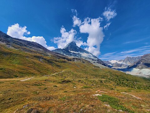 View of the Matterhorn mountain peak rising above alpine meadows and rocky slopes under a clear blue sky in Zermatt, Valais, Switzerland.