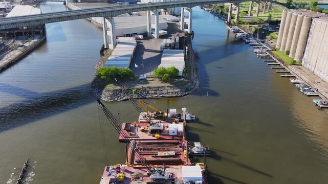 Aerial view of crew teams rowing under the Buffalo Skyway past construction barges and industrial grain silos on the Buffalo River in Buffalo, New York, United States.