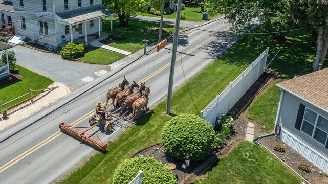 Aerial view of a horse-drawn agricultural implement being pulled along a rural road in the USA.