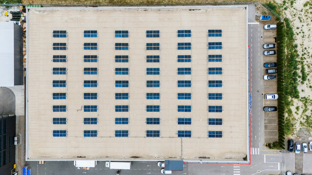 Aerial view of a large warehouse roof featuring rows of solar panels, with a parking area and vehicles visible below in Novi Sad, Vojvodina, Serbia.