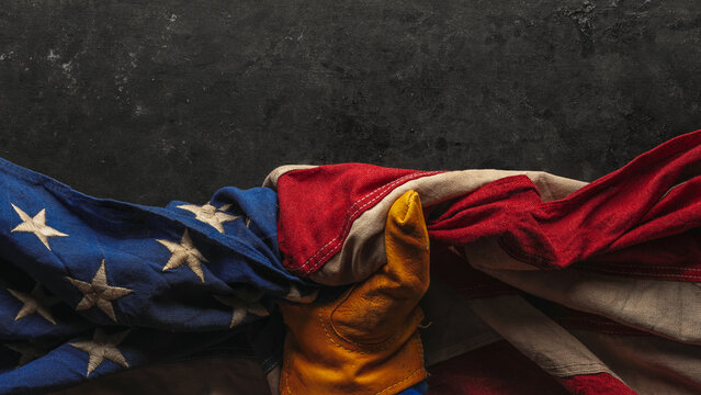 Hand in worn work glove holding the American flag. Symbolic of hardworking blue collar workers, USA manufacturing, pride in products Made in United States of America, or to celebrate US Labor Day.