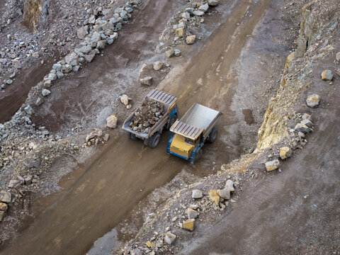 Aerial view of two heavy-duty dump trucks driving along a dirt road in a rocky quarry in Krakow, Lesser Poland Voivode, Poland.