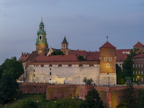 Aerial view of Wawel Royal Castle featuring historic stone walls, towers, and red-tiled roofs illuminated at dusk in Krakow, Lesser Poland Voivode, Poland.