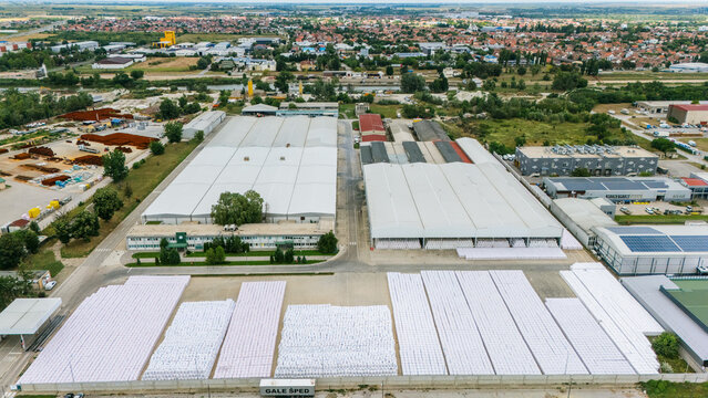 Aerial view of a large industrial warehouse facility with rows of white storage bags in the yard, surrounding buildings, and green spaces in Novi Sad, Vojvodina, Serbia.